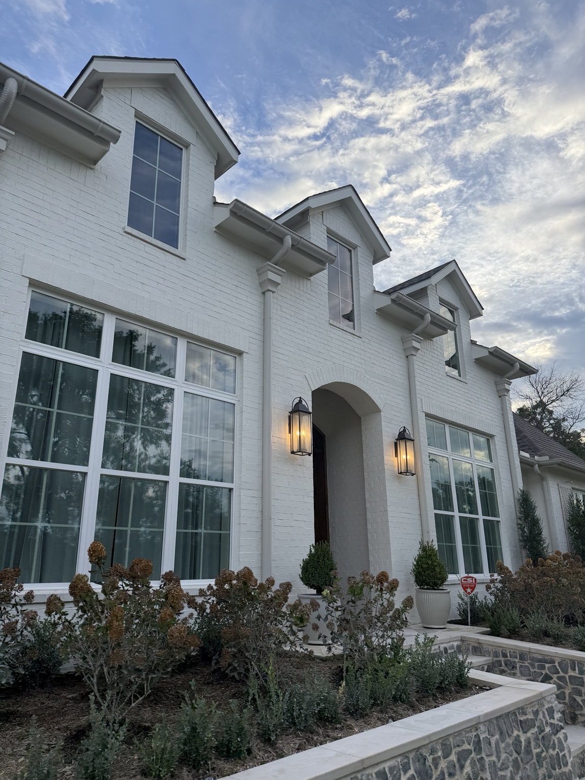White brick home with tall windows and reflected clouds